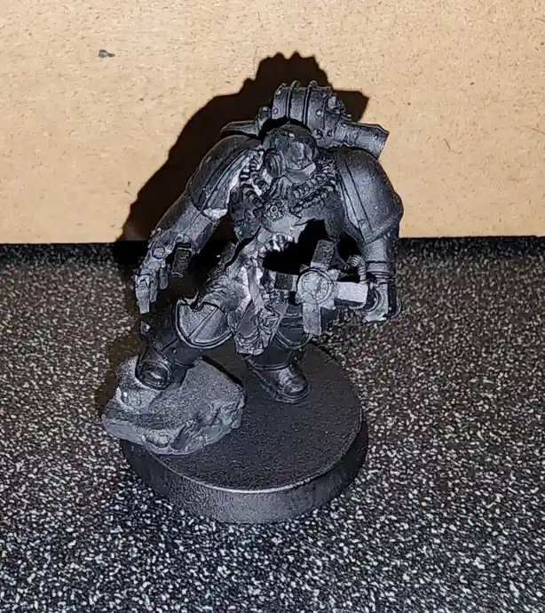 A heavily armored, grey-painted miniature figure, likely from Warhammer 40,000, stands on a circular base with one foot on a…