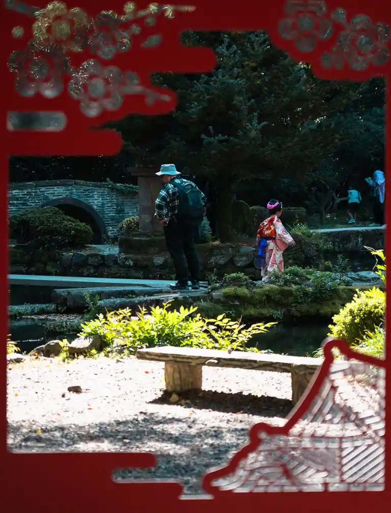 A man in a plaid shirt and backpack stands beside a young girl in a colorful kimono in a traditional Japanese garden with…