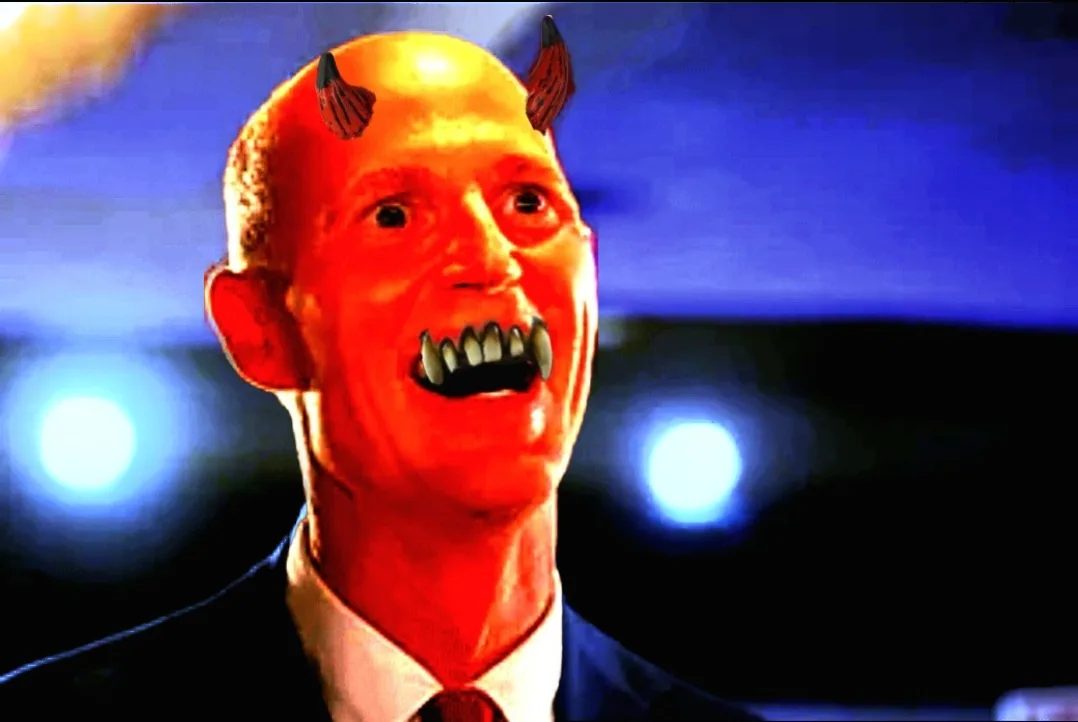 A man in a suit and tie is digitally edited to have small devil horns and sharp fangs, with his face bathed in red light…