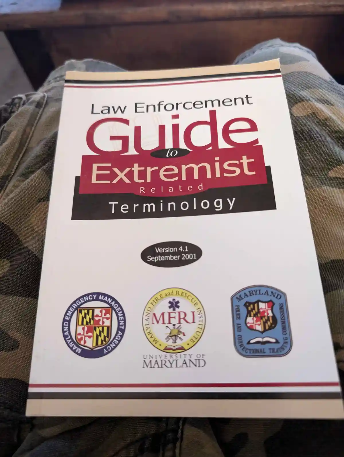 A person is holding a white booklet titled 'Law Enforcement Guide to Extremist Related Terminology', version 4.1 from…