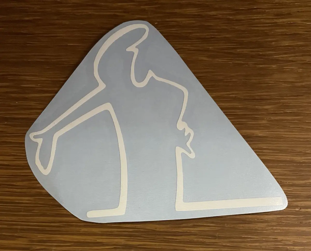 A light gray, triangular-shaped sticker with a white outline of a person in a golfing stance is placed on a wooden surface…