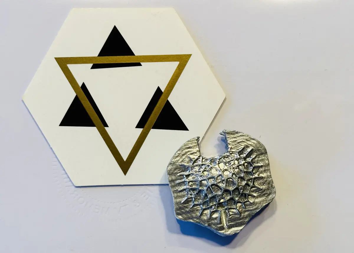 A white hexagonal sticker with a gold outline and black triangles forming a Star of David is placed next to a textured…