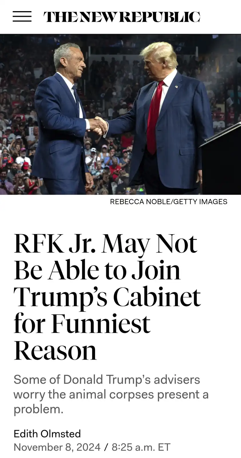 The image shows two men in suits shaking hands on a stage in front of a crowd. The man on the left is Robert F. Kennedy Jr…