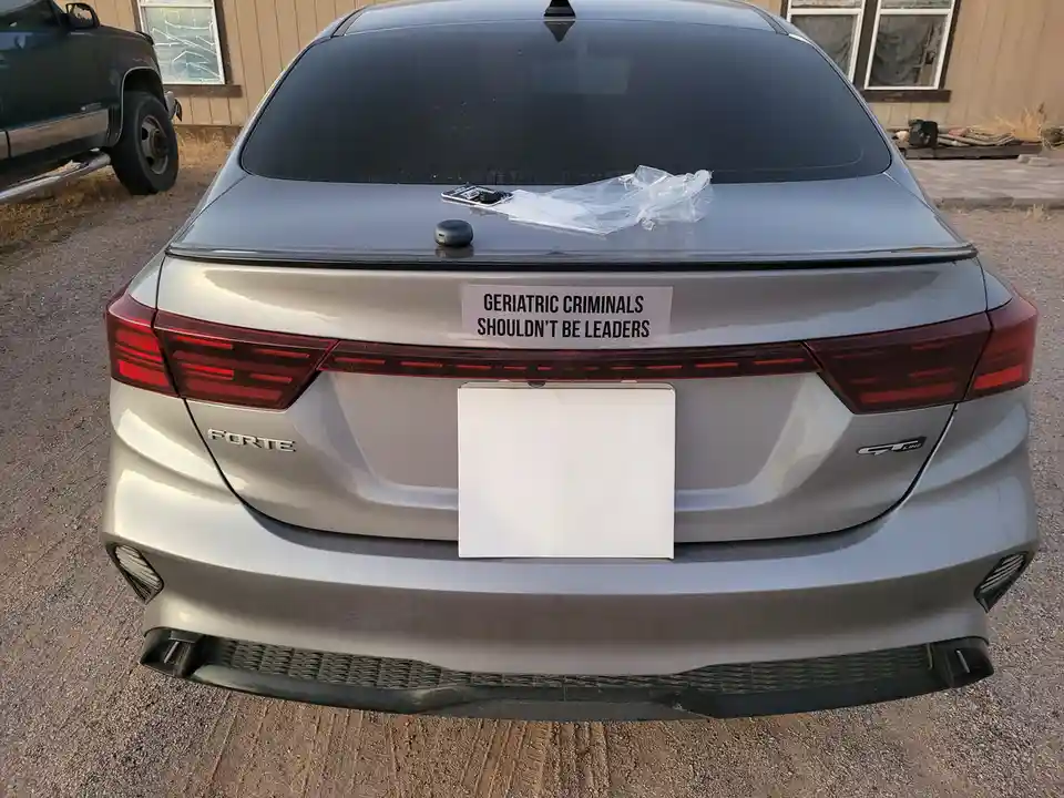 The rear view of a silver Hyundai Forte GT-Line sedan parked outdoors, featuring a white license plate and a handwritten…