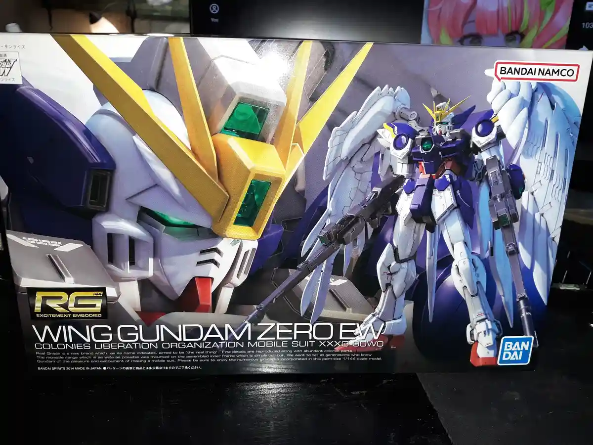 The image shows a Bandai Real Grade model kit box for the Wing Gundam Zero EW, featuring a large close-up of the robot's…