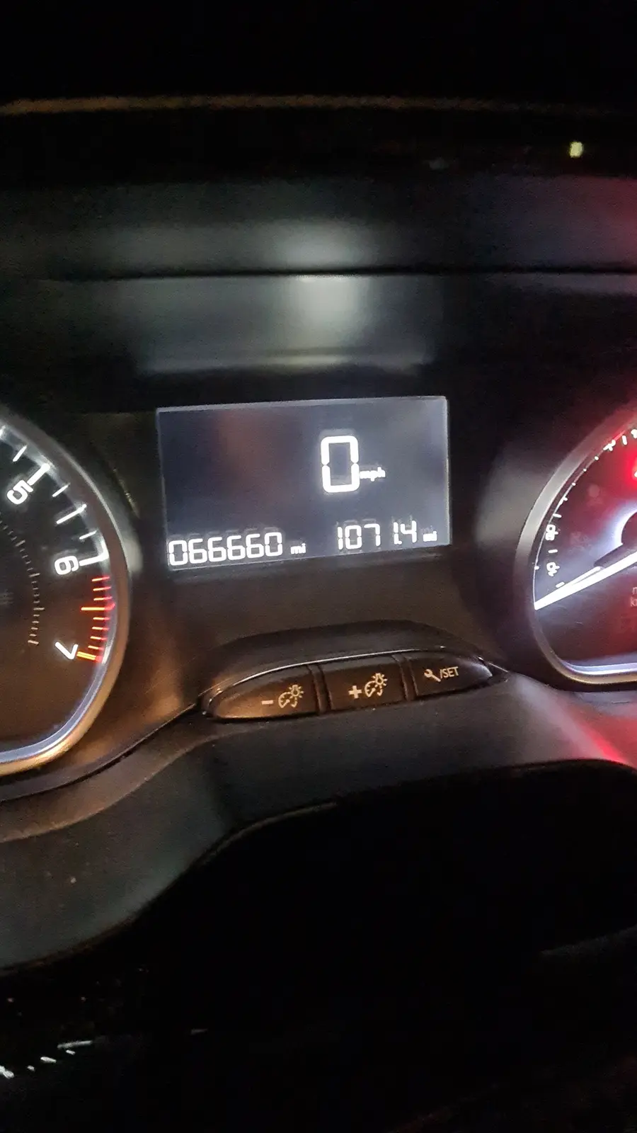 A close-up of a car's digital dashboard at night, showing the speedometer at 0 mph, total mileage at 66,660 miles, and trip…
