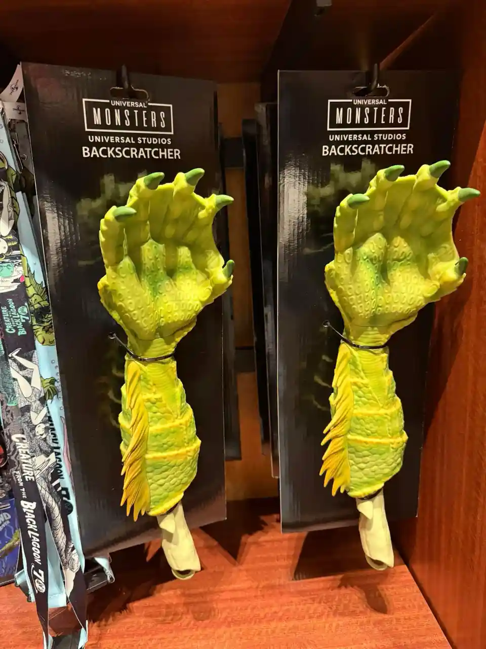Two identical green, clawed monster hands with textured skin and long nails are displayed as 'Backscratchers' in Universal…