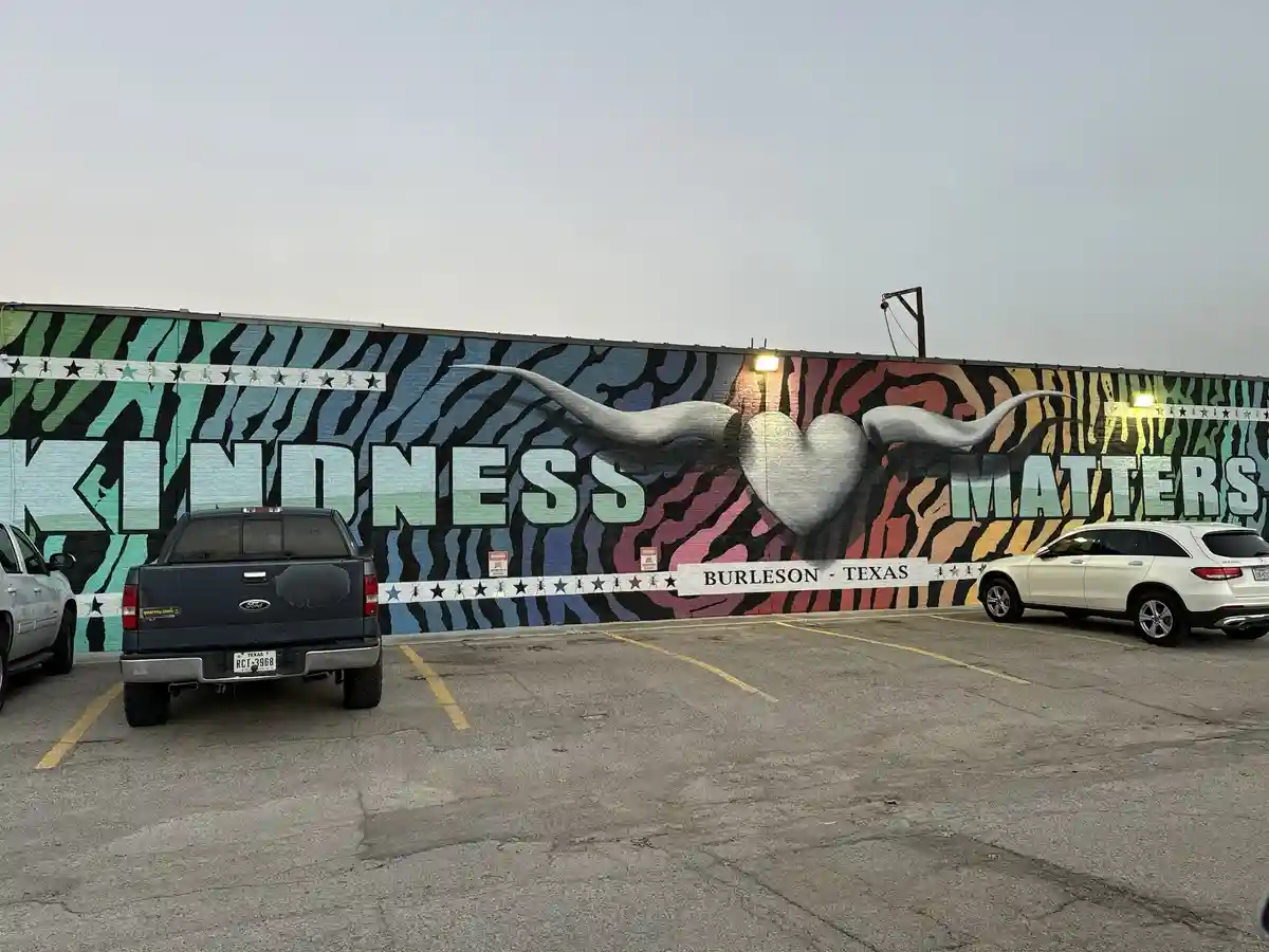 A large, colorful mural on a building wall in Burleson, Texas, features the words 'KINDNESS MATTERS' in large block letters…