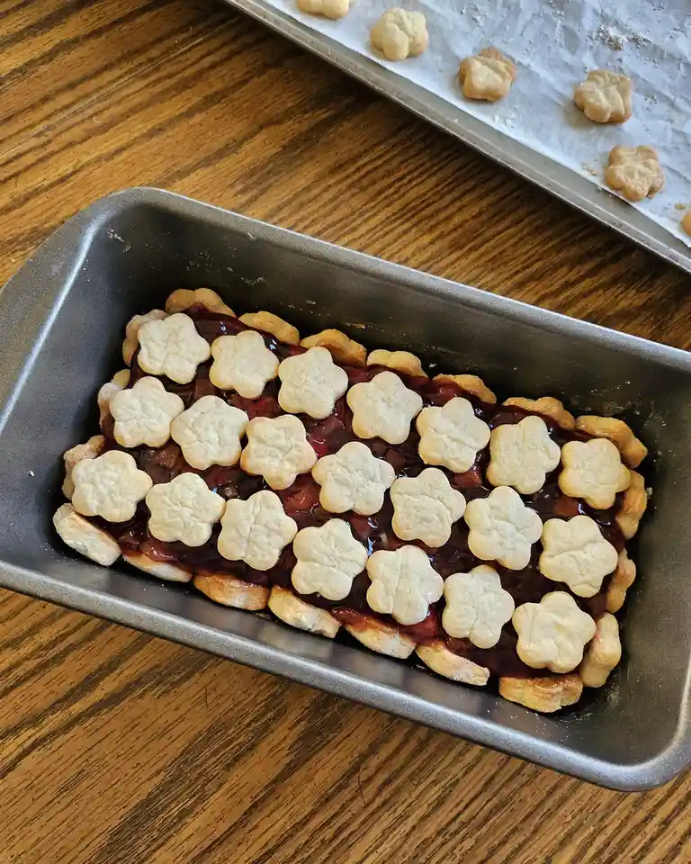 A loaf pan contains a dessert made of a layer of dark red jam or fruit filling, topped with rows of star-shaped…
