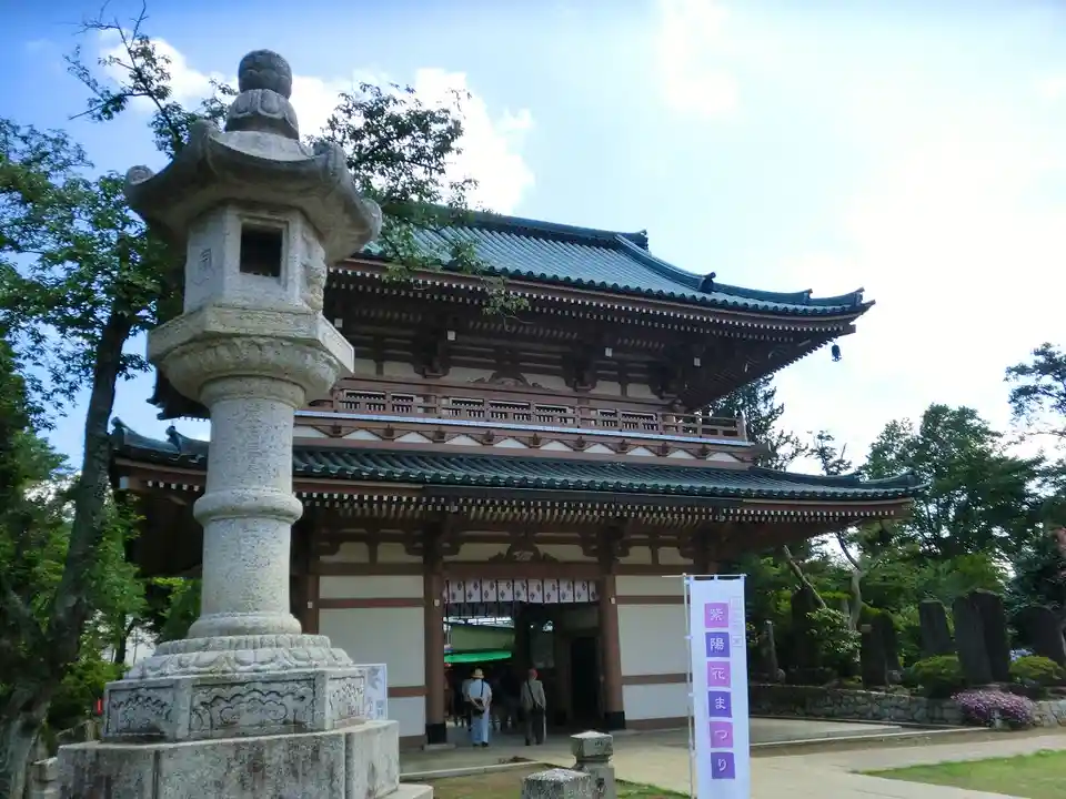 A traditional Japanese temple with a large stone lantern in the foreground, under a partly cloudy sky. The temple has a…