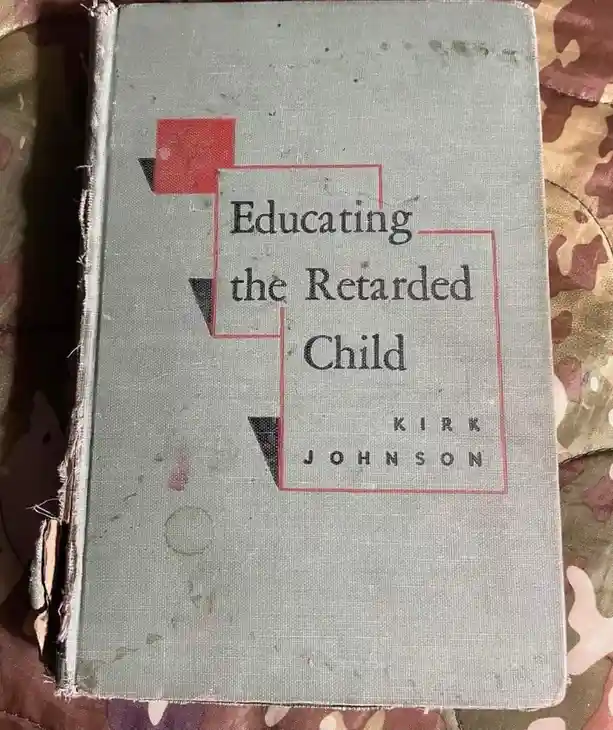 A worn, light green book with a faded cover titled 'Educating the Retarded Child' by Kirk Johnson, featuring abstract red…