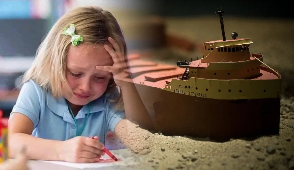 A young girl with blonde hair and a green bow, wearing a blue shirt, looks distressed while holding her head with one hand…