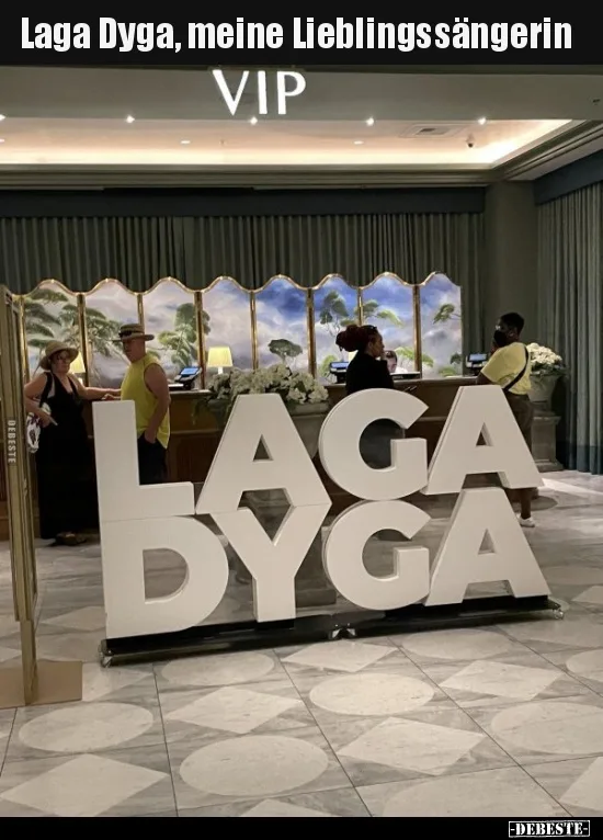 A photo of a hotel lobby with a large white 'LAGA DYGA' sign on the floor. People are standing around a reception desk with…