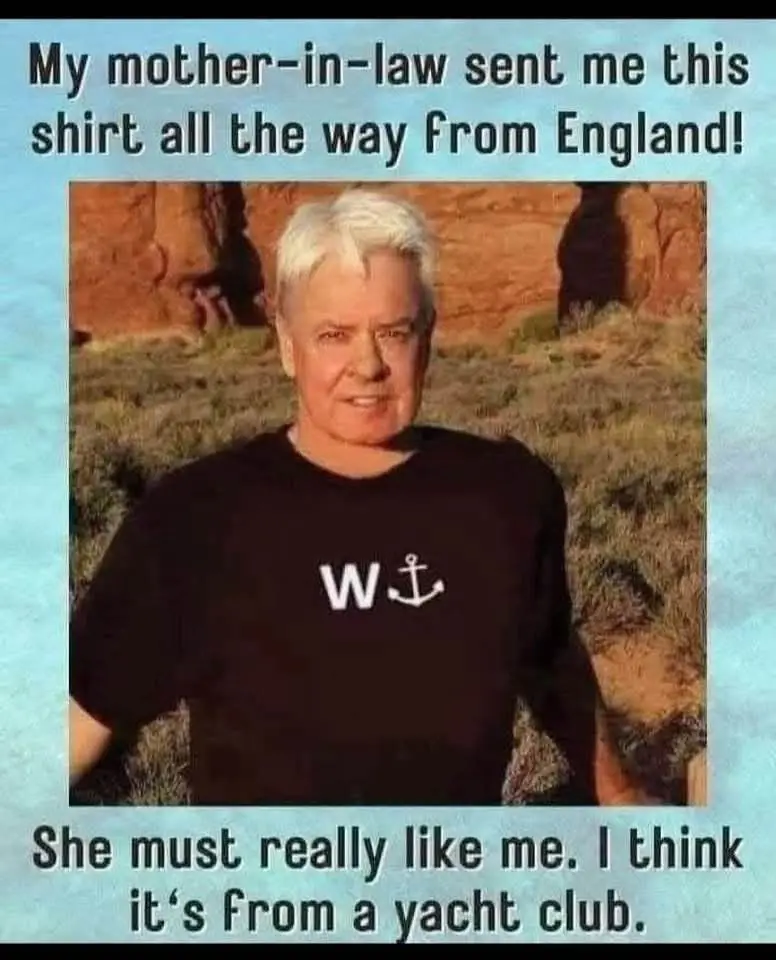 A man with white hair stands outdoors in front of red rock formations, wearing a black t-shirt with a white 'W' and anchor…