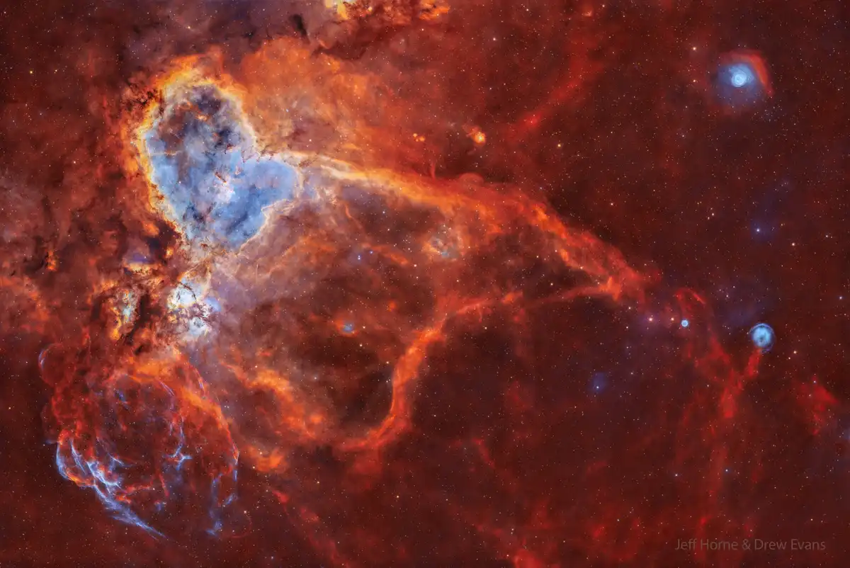 A vibrant space nebula image with swirling red, orange, and blue clouds of gas and dust against a starfield, featuring the…