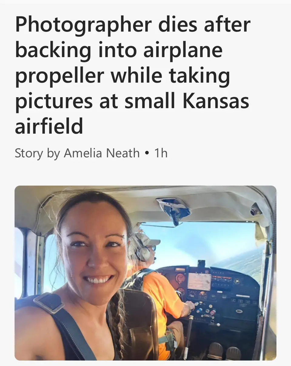 A smiling woman takes a selfie in the cockpit of a small airplane, with a pilot in an orange shirt visible behind her. The…
