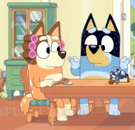 A still from the animated show 'Bluey' shows two cartoon dogs, Bluey and Bingo, sitting at a wooden dining table. A small…