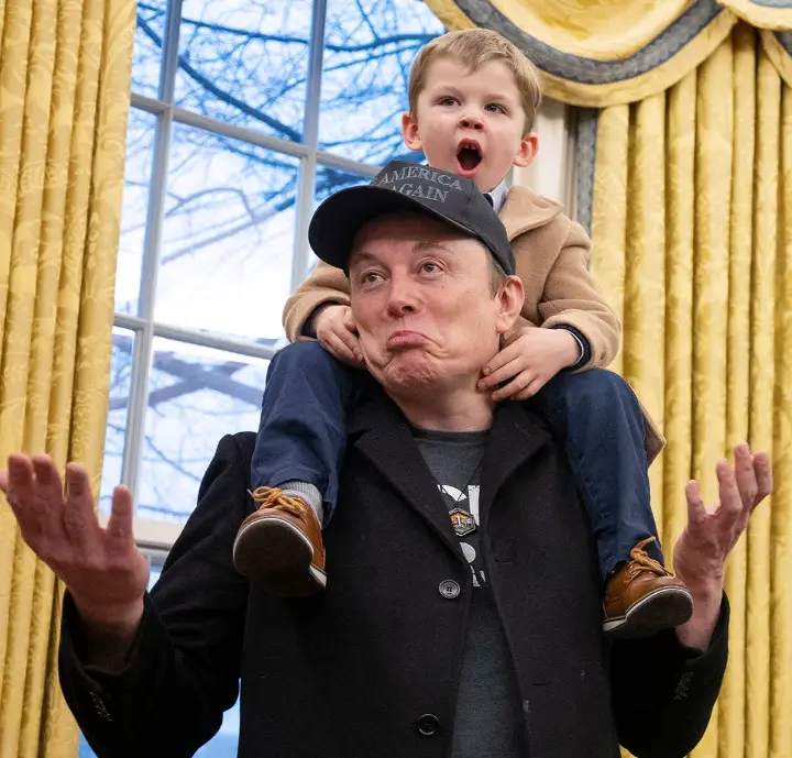 A man wearing a black 'America Again' cap and a dark coat has a young boy perched on his shoulders. The boy, in a tan coat…