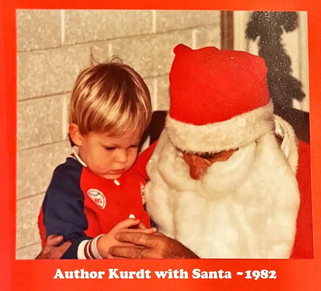 A vintage, slightly grainy photo shows a young blond boy in a red and blue outfit sitting beside a man dressed as Santa…