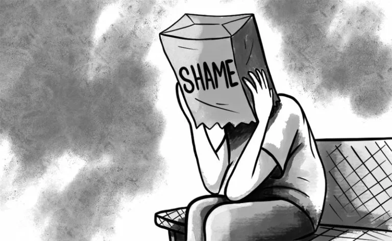 A black-and-white cartoon depicts a person sitting on a bench, covering their head with a large paper bag labeled 'SHAME'…