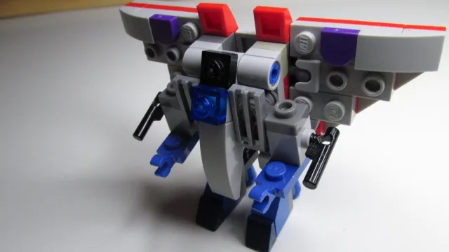A gray, blue, and red Lego robot stands on a white surface, constructed from various interlocking pieces with visible studs…