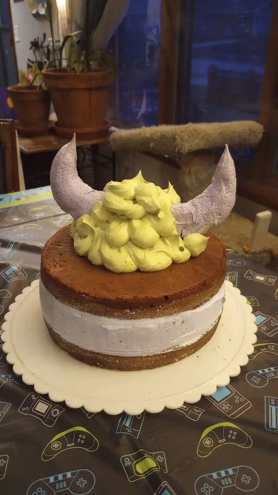 A two-layer cake with brown cake layers and white frosting sits on a white scalloped cake stand. The top is decorated with a…