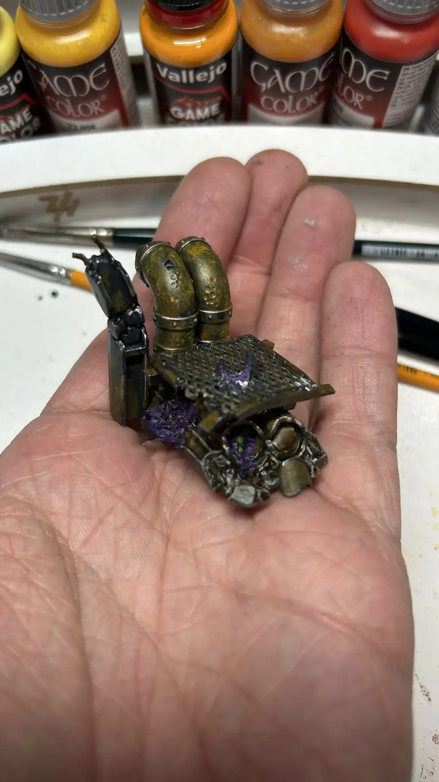 A hand holds a small, intricately painted miniature model, likely a sci-fi or fantasy piece, featuring metallic textures and…