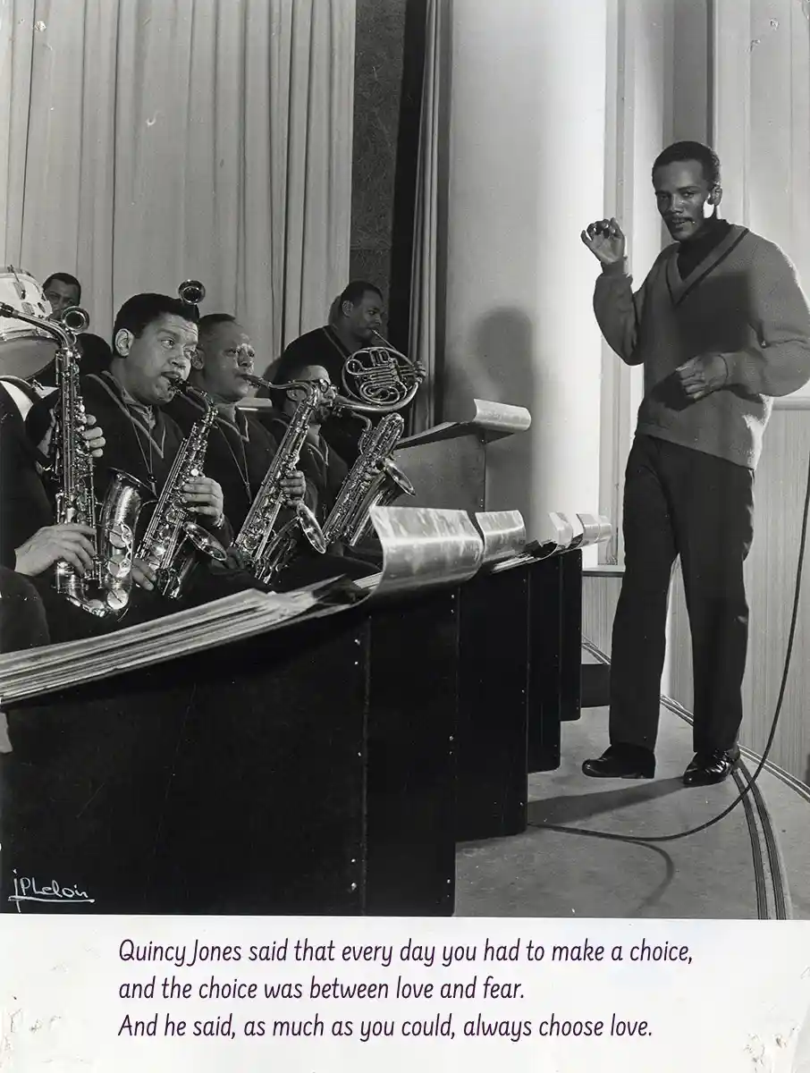 A black-and-white photo shows Quincy Jones standing and gesturing while a band of musicians, mostly playing saxophones and a…