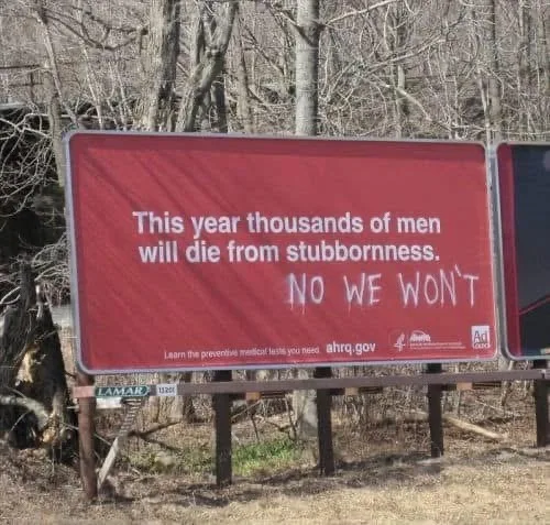 A red public service announcement billboard with white text reads 'This year thousands of men will die from stubbornness.'…