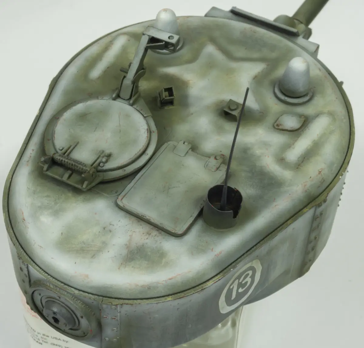A close-up of a weathered, olive-drab military helmet with various metal fittings, a circular hatch, and a small…