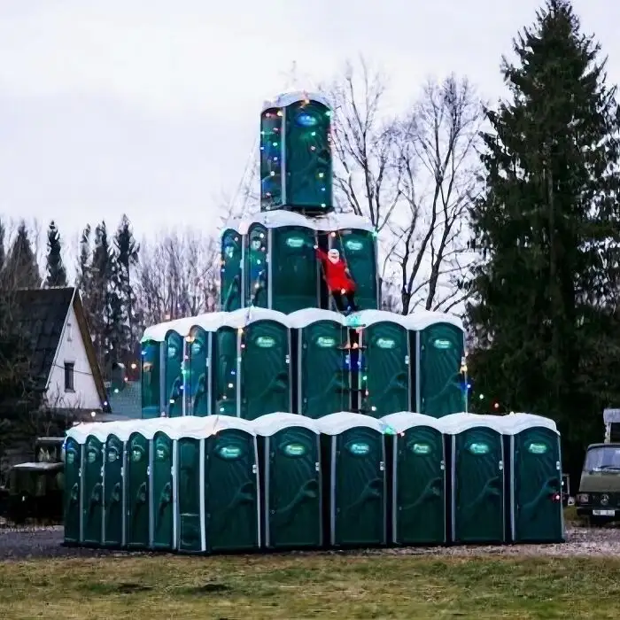 A person dressed as Santa Claus is climbing a large pyramid made of green portable toilets, which are decorated with string…