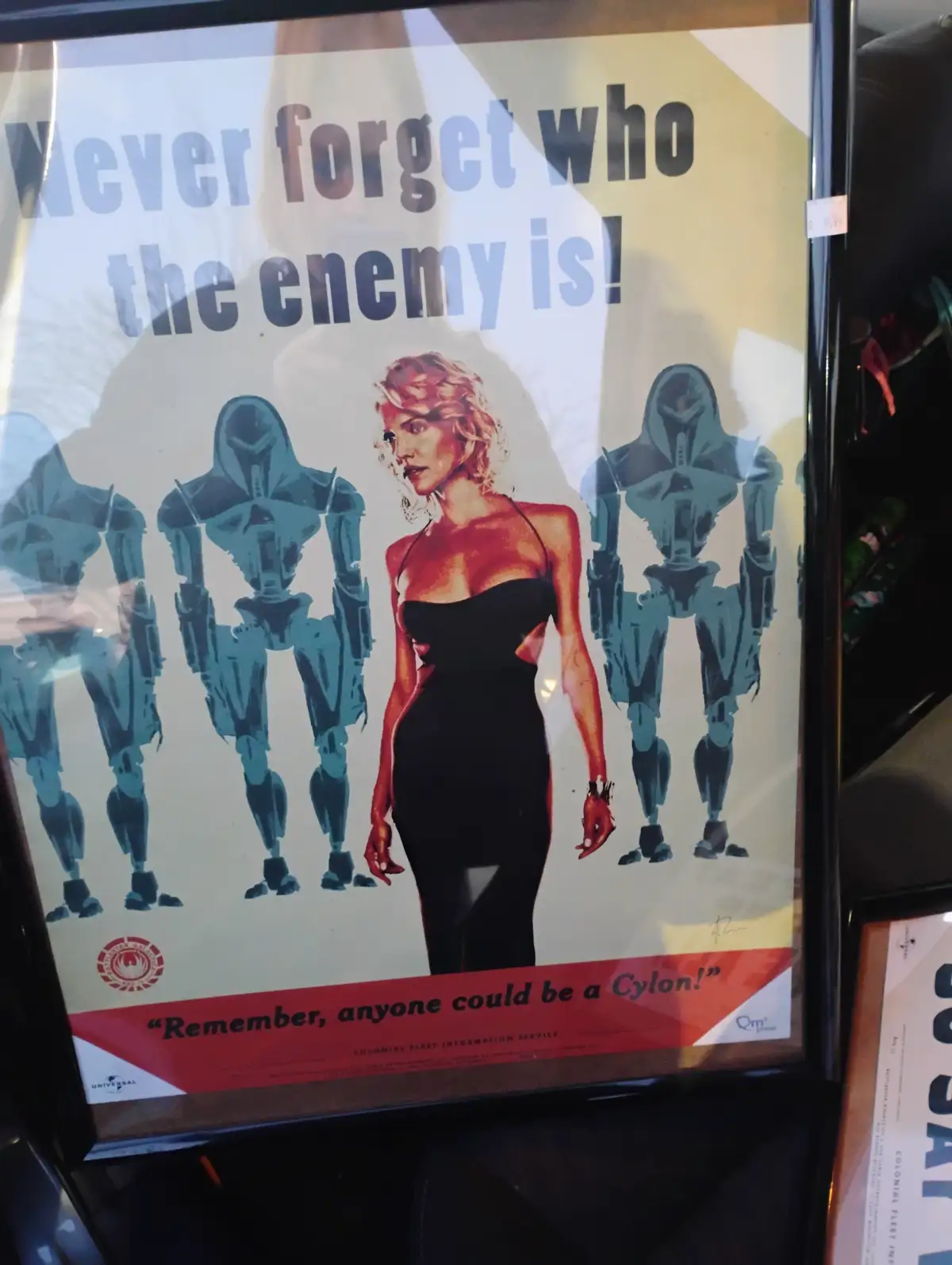 A framed propaganda-style poster featuring a blonde woman in a black dress standing between four menacing blue Cylon…