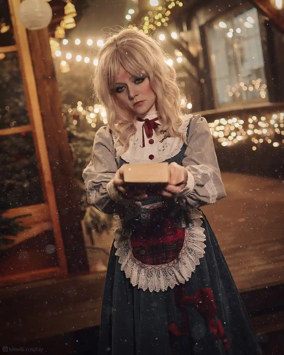 A person in a detailed Victorian-style dress with red bows and lace holds a small wrapped gift box while looking directly at…
