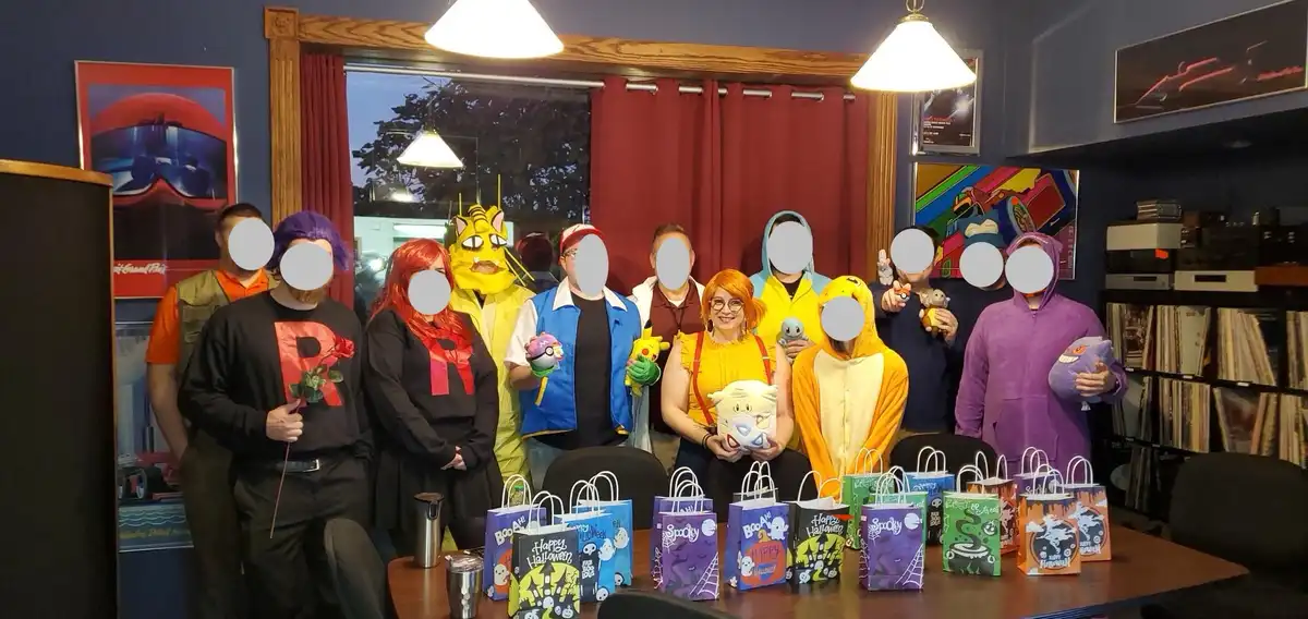 A group of people in Pokemon-themed costumes, including Team Rocket members and various Pokemon characters, stand behind a…