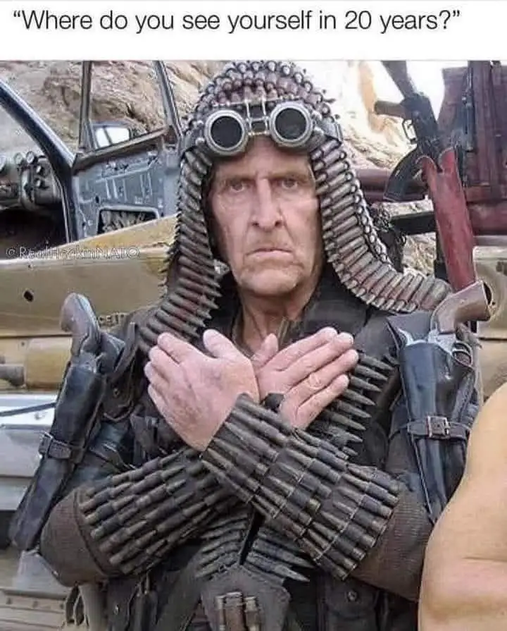 A man in a post-apocalyptic outfit with bandoliers of bullets wrapped around his head, arms, and torso, wearing goggles, and…