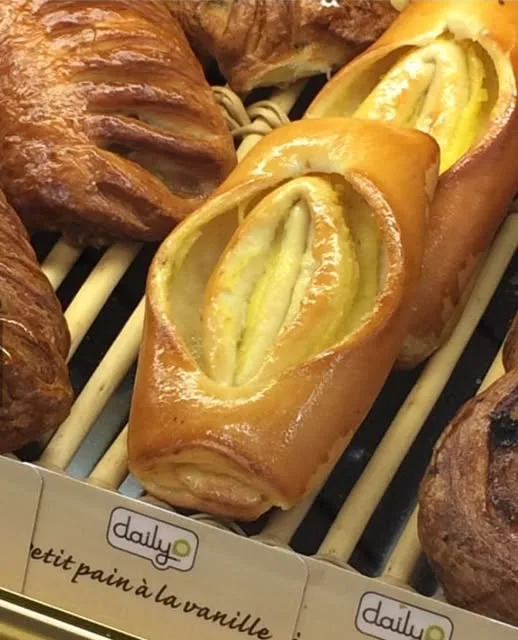 A close-up photo of golden-brown pastries on a wooden slatted tray, with one pastry in the foreground having a split, curved…