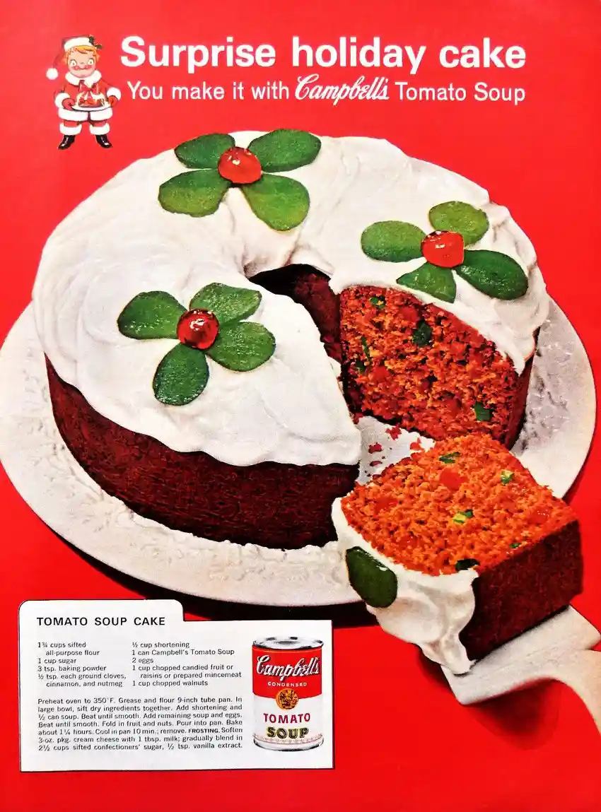 A vintage Campbell's advertisement shows a round, red-orange cake with white frosting and green holly decorations, with a…
