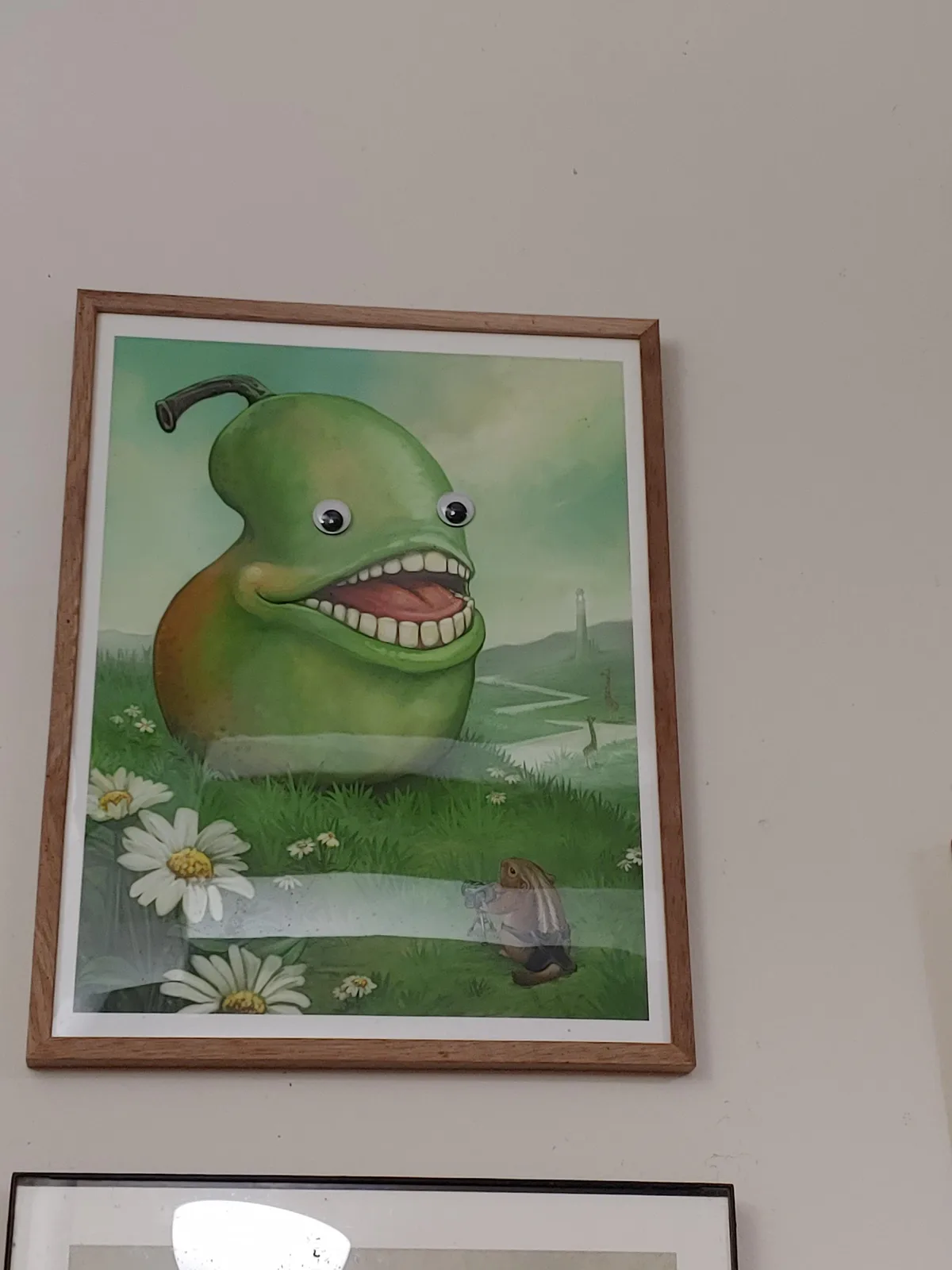 A framed painting depicts a large, anthropomorphic green pear with googly eyes and a wide, toothy grin, standing in a grassy…