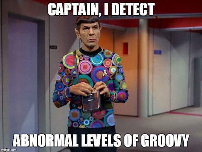 A man dressed as Spock from Star Trek stands in a hallway, wearing a colorful shirt with concentric circles, holding a…
