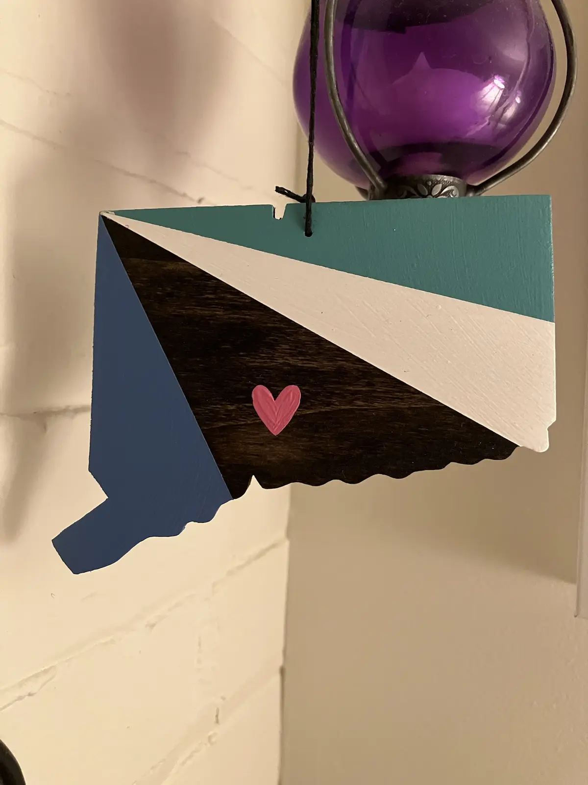 A wooden cutout shaped like the state of New Hampshire is painted with the colors of the bisexual pride flag: teal, white…