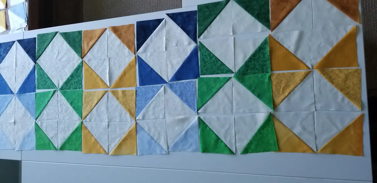 A photo shows a quilt pattern laid out on a white surface, composed of many small fabric triangles in blue, green, white…