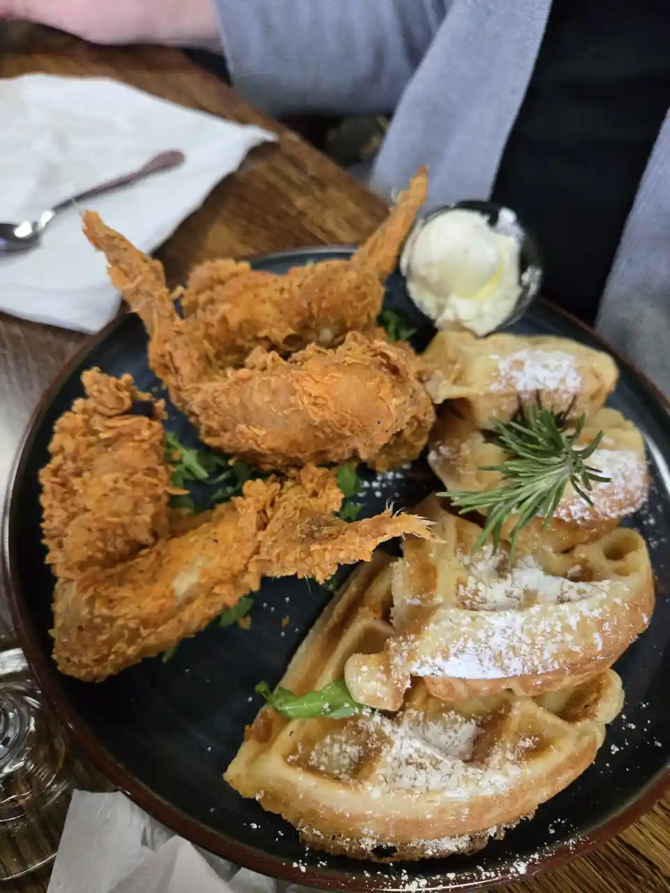 A plate of golden-brown fried shrimp with crispy batter sits next to a stack of waffles dusted with powdered sugar and…