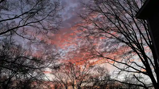A photograph shows a dramatic sky at sunset or sunrise, with clouds glowing in fiery orange and pink hues against a darker…