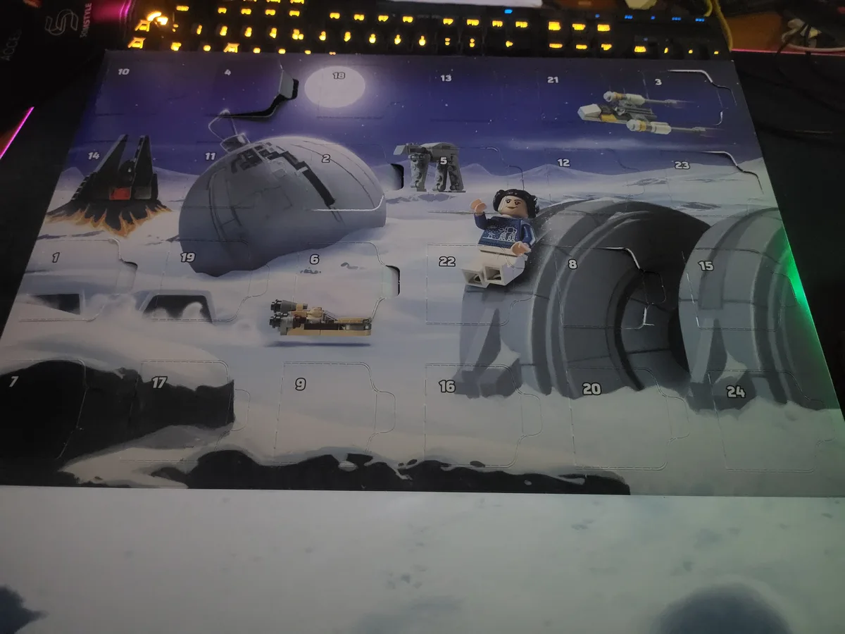 A partially opened LEGO Star Wars Advent Calendar featuring a snowy Hoth landscape with numbered compartments. Several…