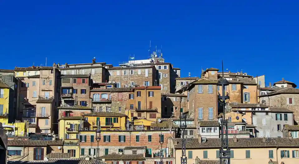 A scenic photo of densely packed, colorful European-style buildings with terracotta roofs under a clear blue sky, overlaid…