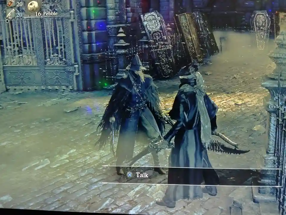 Two hooded, darkly dressed characters stand facing each other in a gothic, cobblestone courtyard with ornate gates and…