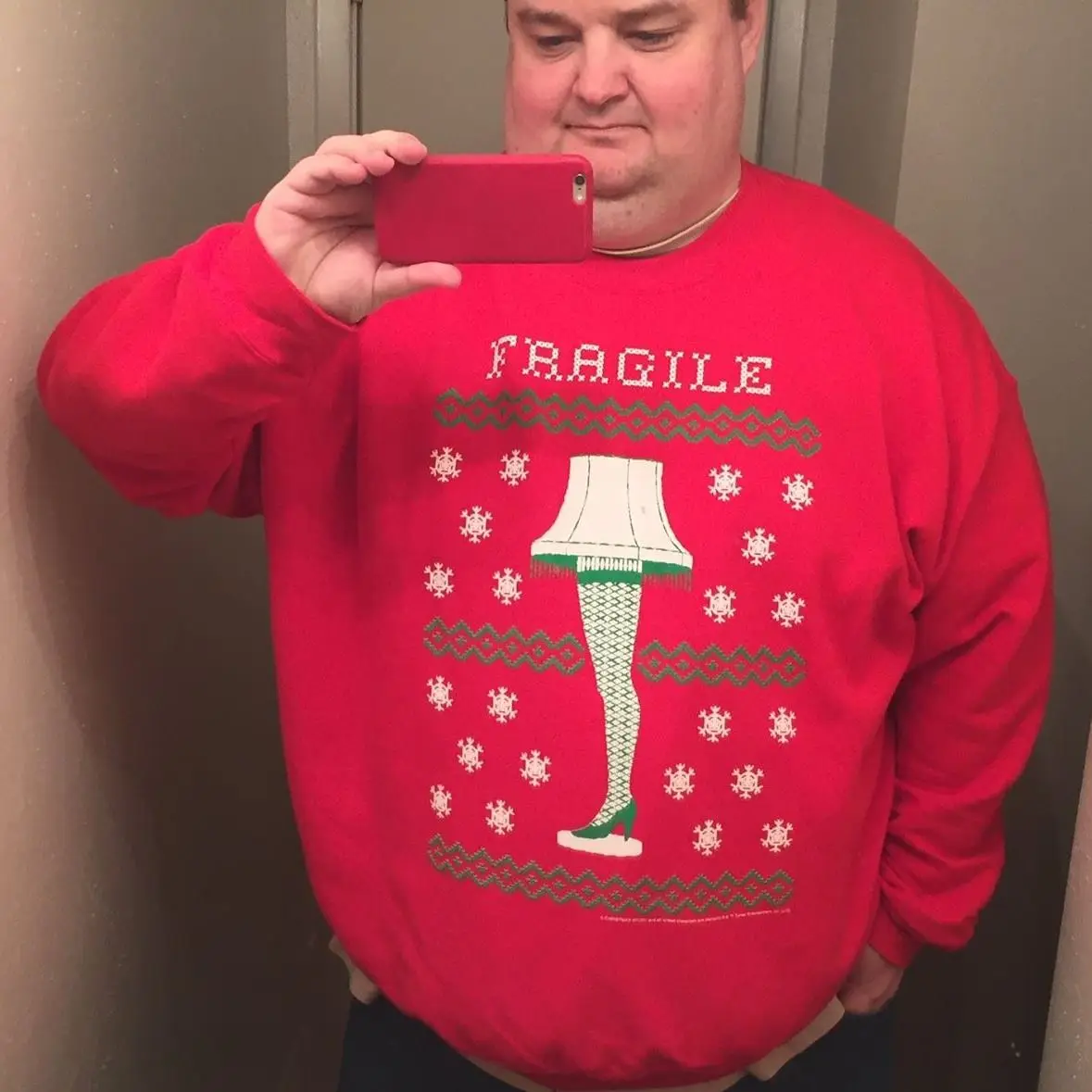 A man in a red christmas sweater with a graphic of the leg lamp from 'A Christmas Story' and the word 'FRAGILE' above it…