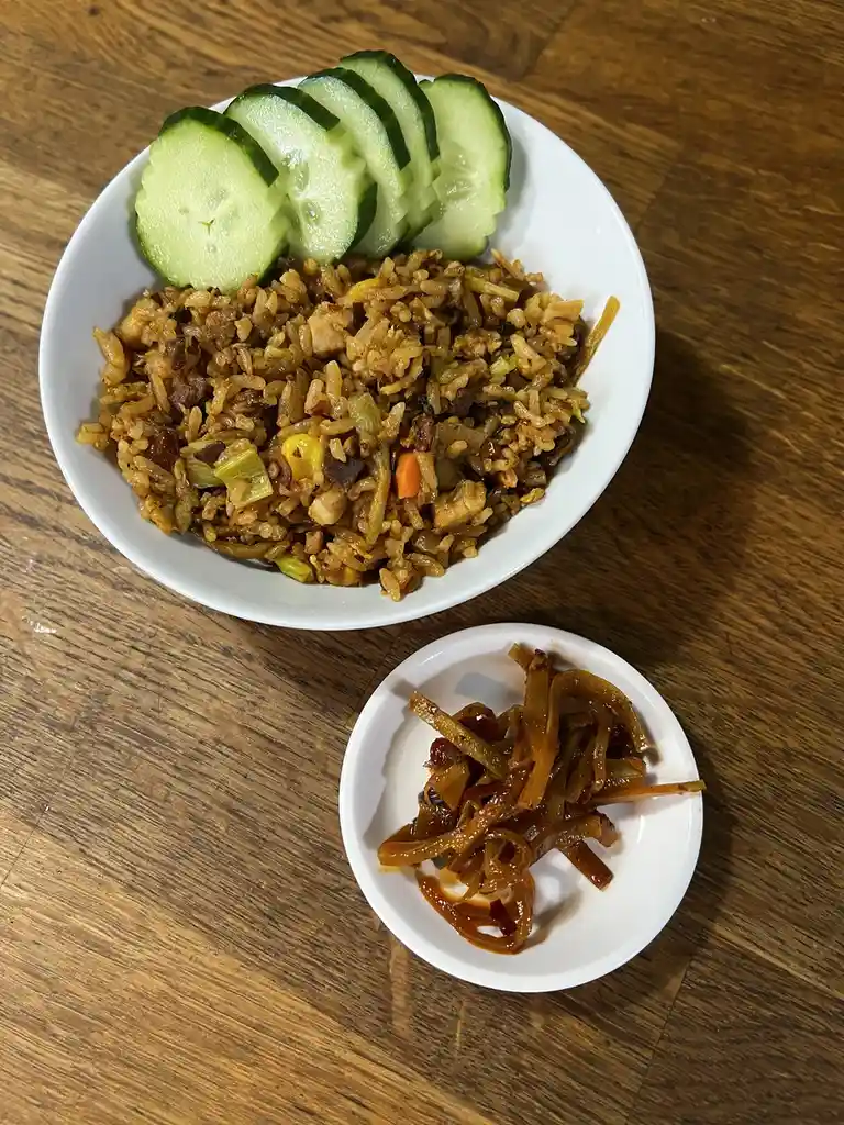 A top-down photo shows a white bowl of fried rice with visible ingredients like corn, carrots, and meat, topped with sliced…