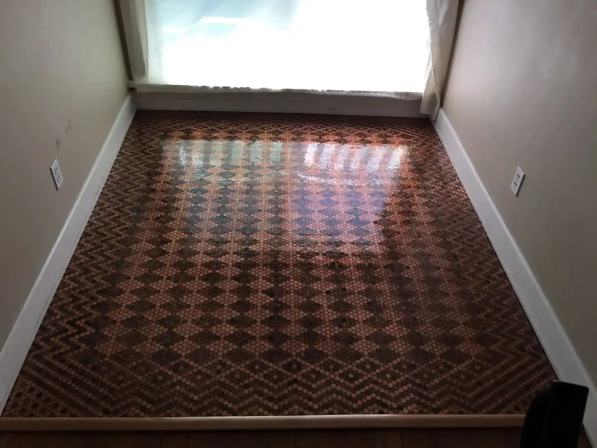 A room's floor is covered with pennies arranged in a geometric pattern, with sunlight streaming in from a window at the far…