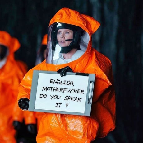 A person in an orange hazmat suit holds a whiteboard with the text 'ENGLISH, MOTHERFUCKER DO YOU SPEAK IT ?'. The individual…